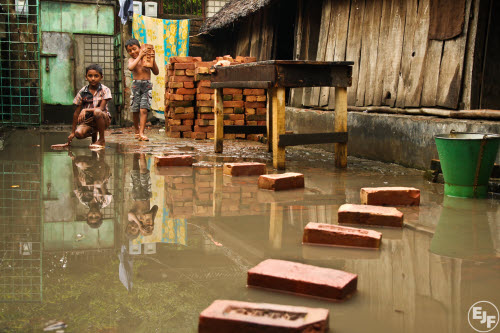 Boys make a path across a flooded slum in Khulna